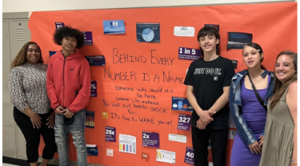 Students and teacher from Mitchell stand in front of a poster with information about gun violence.